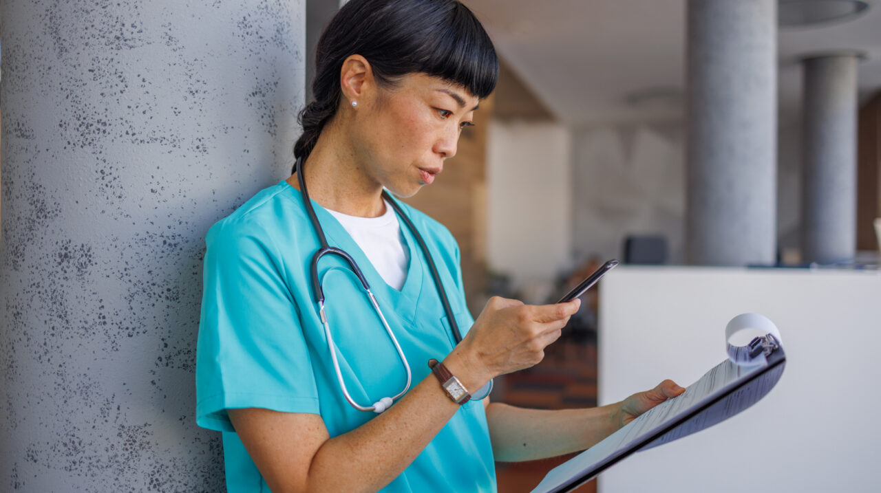 Asian female medical professional is checking patient information on her phone and reading medical report