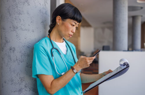 Female doctor using mobile phone and reading medical report in hospital Asian female medical professional is checking patient information on her phone and reading medical report